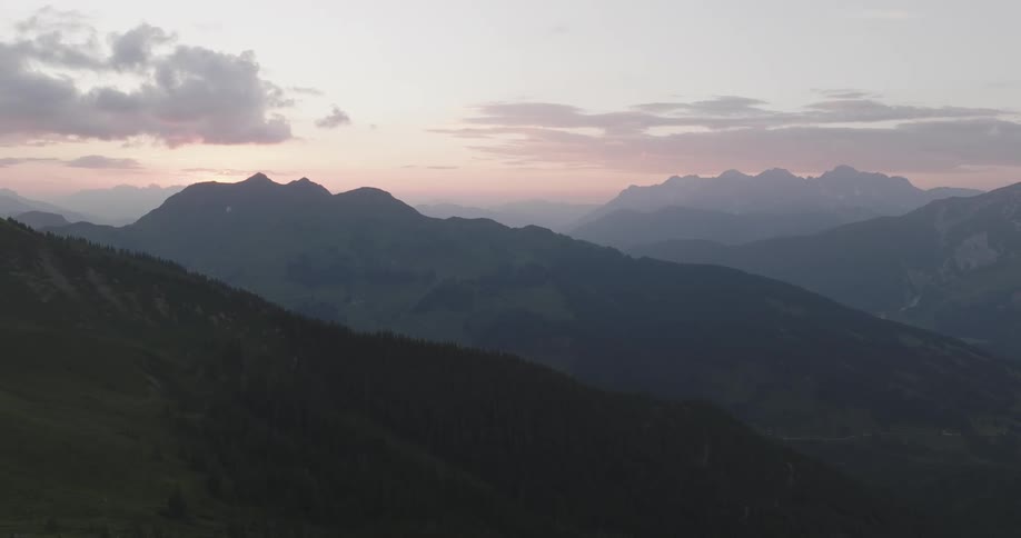 A person sits with a dog on a bench overlooking a serene mountain landscape at dusk with a calm body of water in the foreground