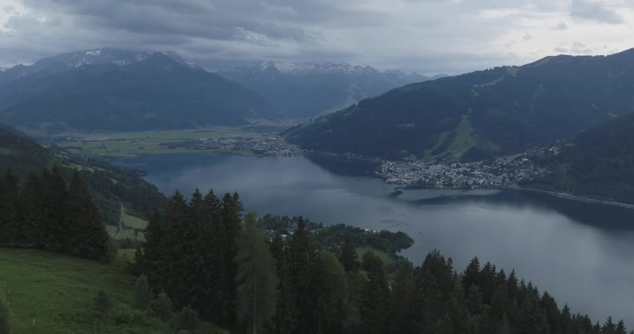 A serene lakeside town nestled amidst snowcapped mountains under low hanging clouds