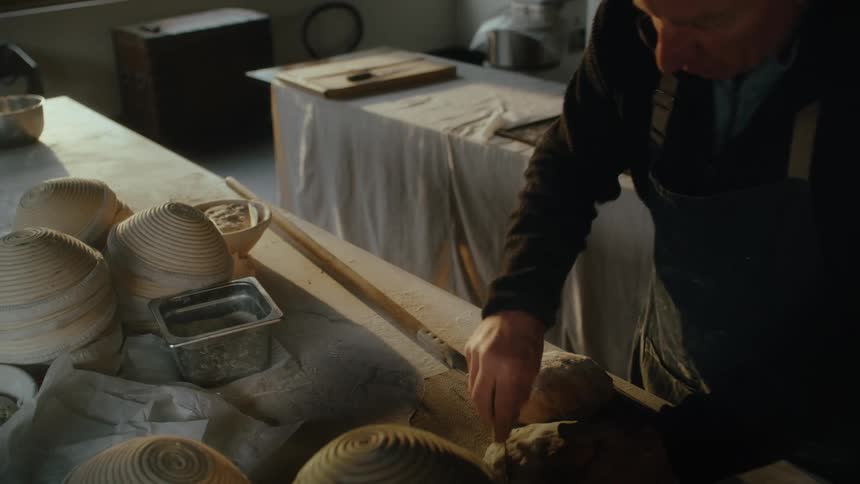 Closeup of hands kneading dough on a floured surface surrounded by bowls of additional dough portions