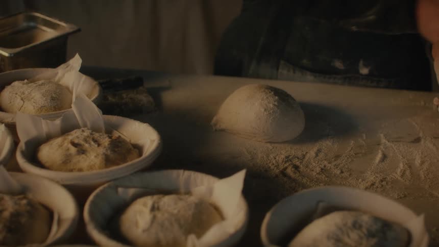 Closeup of hands kneading dough on a floured surface surrounded by bowls of additional dough portions