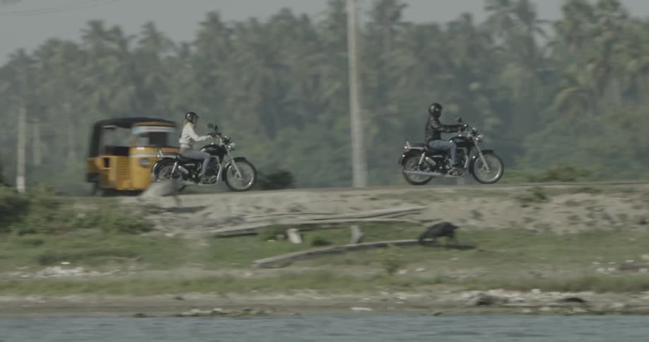 Two people ride motorcycles by the waterfront and over a bridge