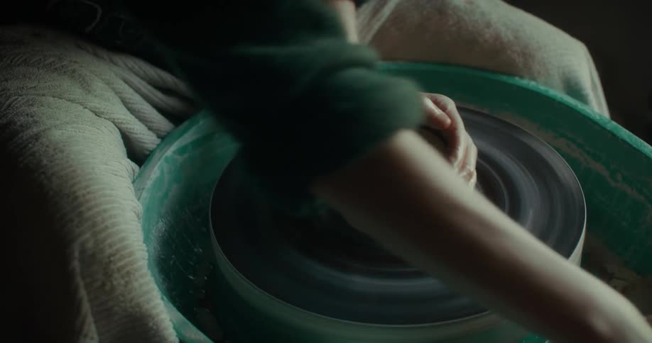 A person is shaping clay on a pottery wheel focusing on their craft