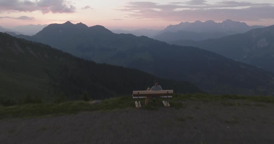 Person sitting on a bench on the peak of a hill overlooking the mountain landscape