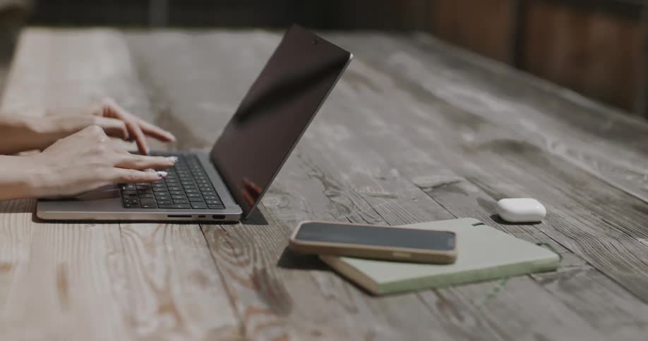 A pair of hands types on a laptop keyboard placed on a wooden surface