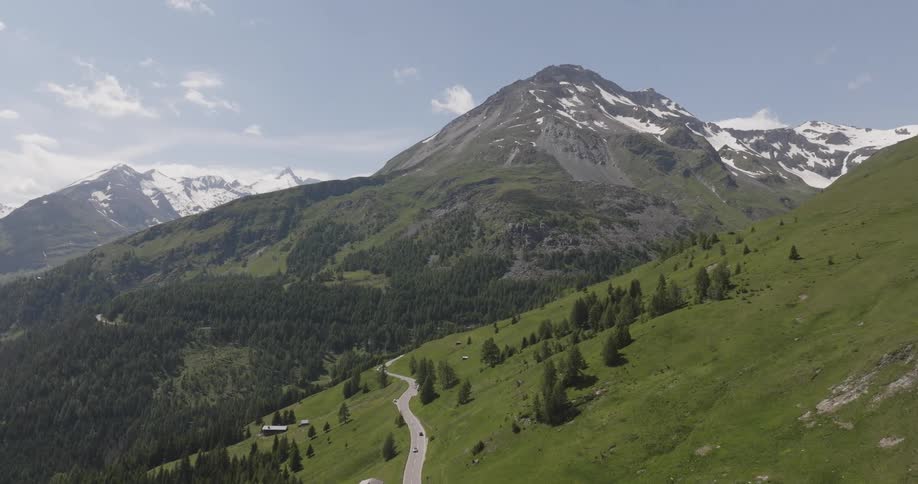 Low aerial view over a road on a green hillside with a large mountain peak in the background on a sunny day