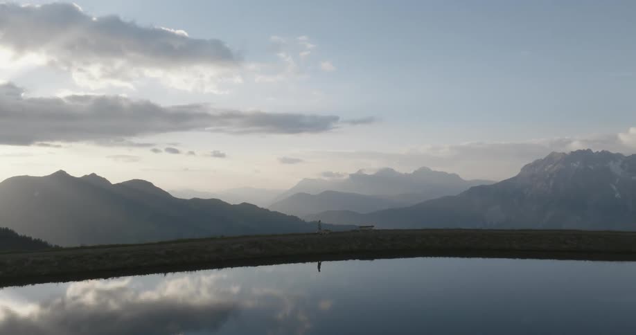 A woman walking a dog on the edge of a lake in the mountains at sunset