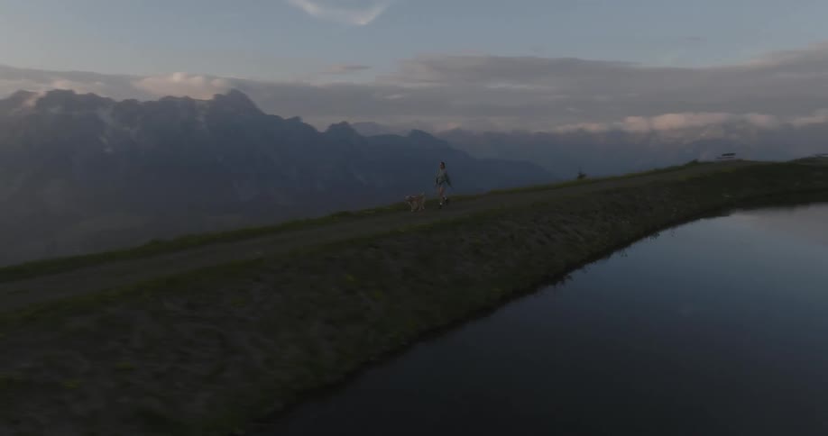 Aerial view of a woman walking her dog near a lake atop the mountains at sunset