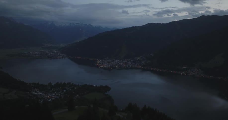 Aerial panorama of green mountains with a lake in the center and an urban city in the background