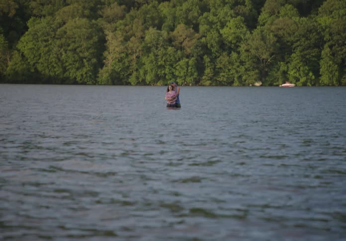 A man and woman embrace while standing in a lake