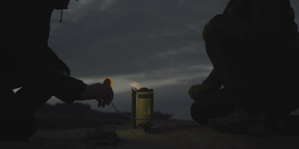 Two people crouch next to a fire inside a canister