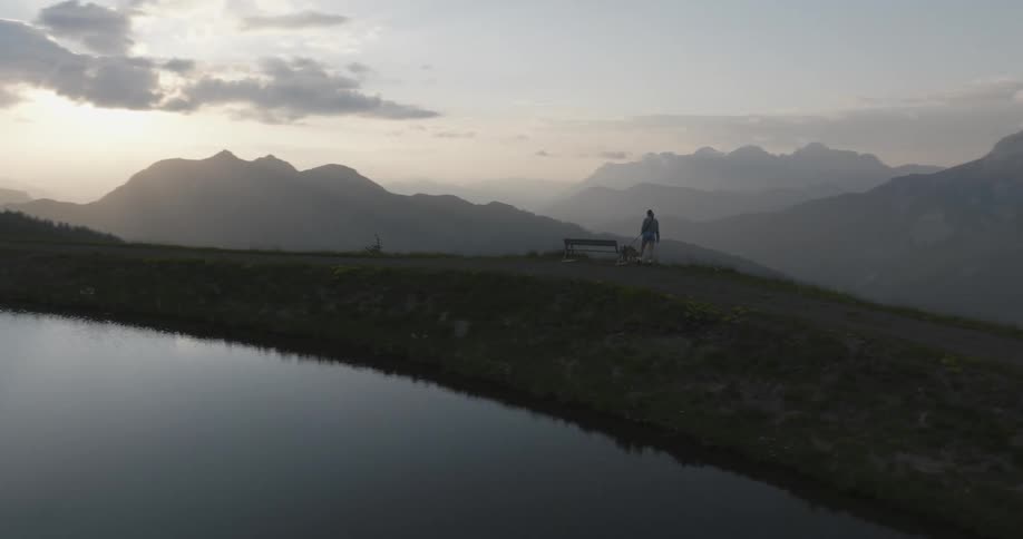 Lake on a hill with a woman in the background walking with her dog in an environment full of mountains at sunrise