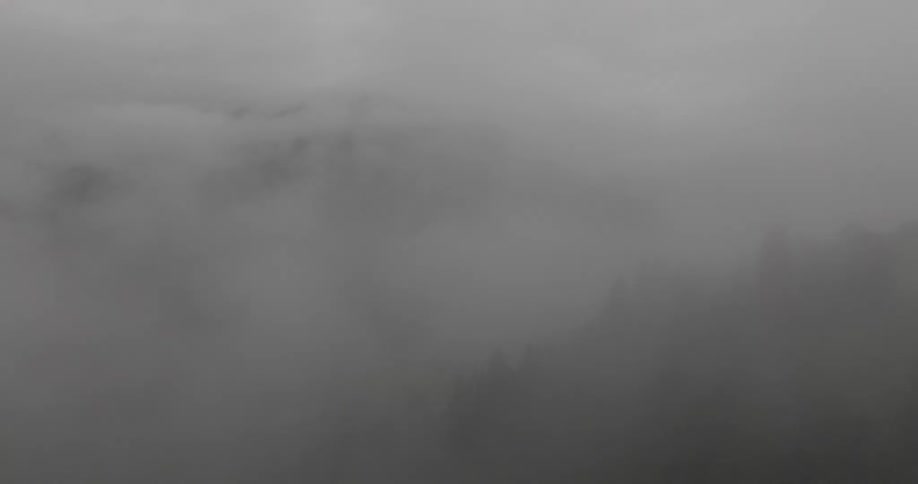 Aerial view of a misty mountain landscape with clouds enveloping forested slopes
