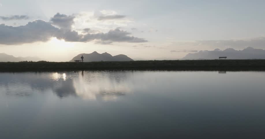 Silhouette of a woman running with a dog around a lake in the mountains