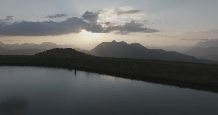 Silhouette of a woman running with a dog at her side against a background of cloudy sky mountains and next to a lake