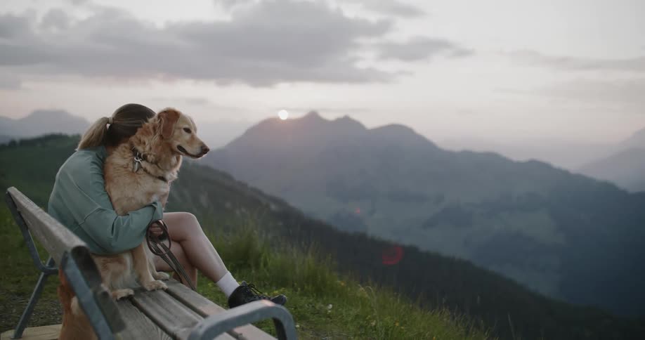 A woman hugs her dog while sitting on a bench on the top of a mountain