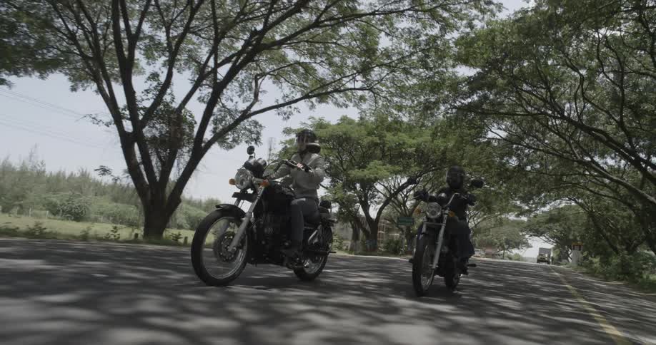 A man and a woman are riding motorcycles down a tree-lined road