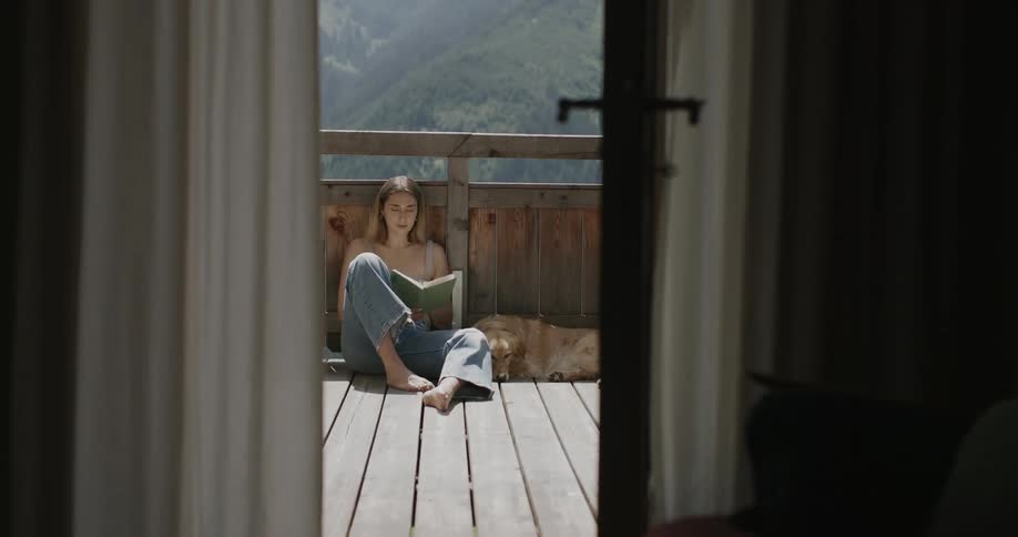 Blonde woman sitting reading a book with a golden retriever by her side