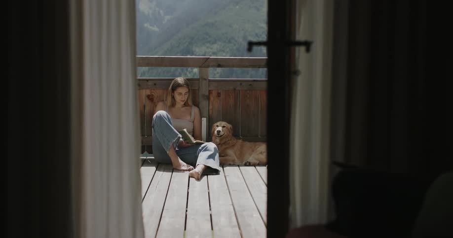 Woman sitting on the porch reading a book and a dog beside her