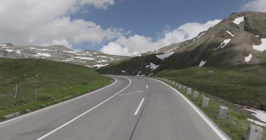 An empty road through a mountainous country side with patches of snow on the ground