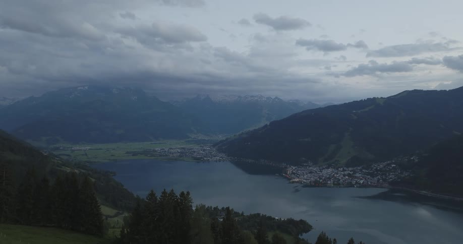A serene lakeside town nestled amidst mountains with clouds hanging low