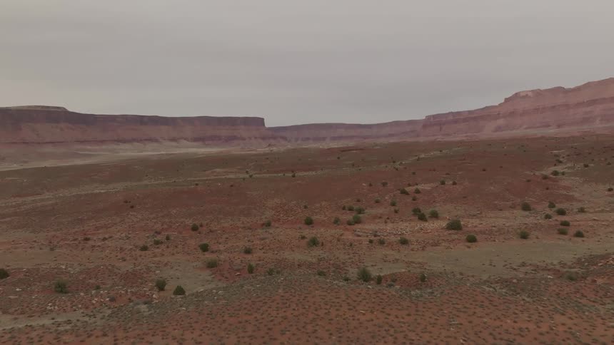 Arid scrub land borders large plateaus under an overcast sky