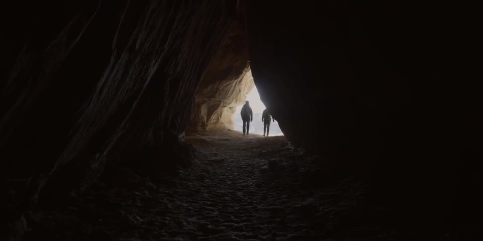 A man and woman walk out of a cave