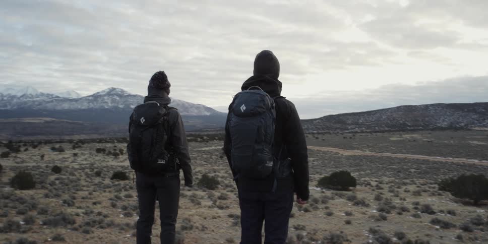 A man and woman stand on a peak looking across a valley