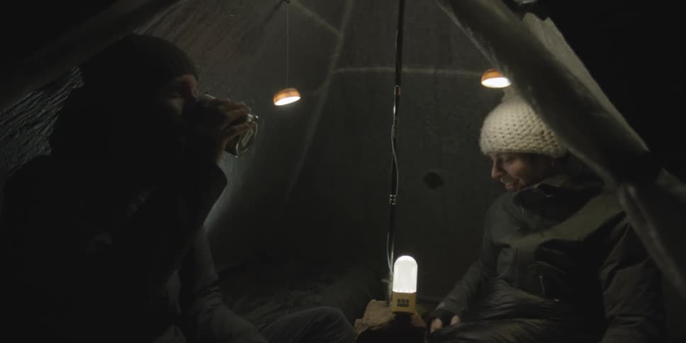 A man and woman sit in a tent near a lightbulb