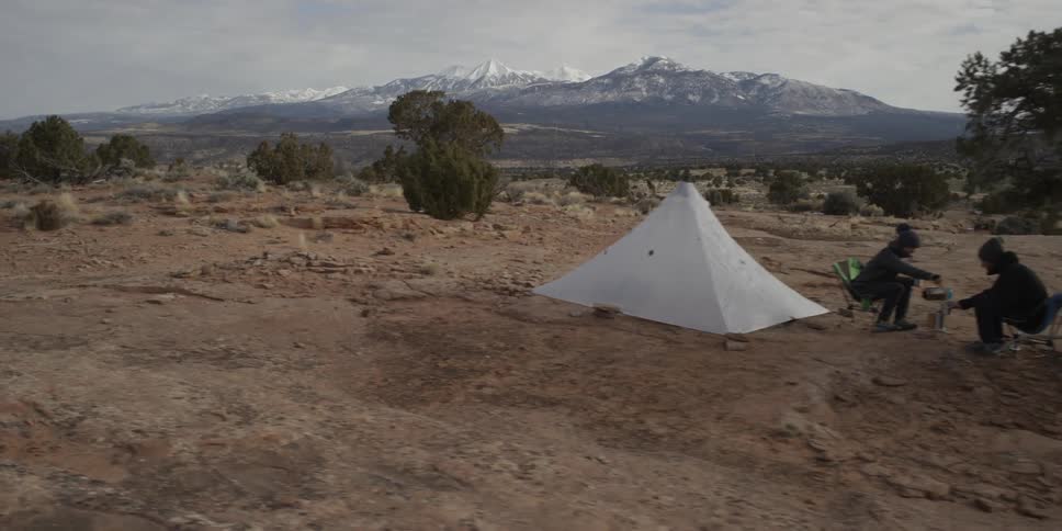 Passing view of two campers sitting on their chairs outside of their tent