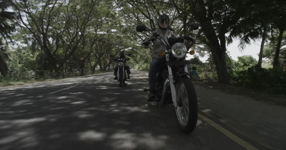 A couple of people riding motorcycles down a country road that is overhung by trees