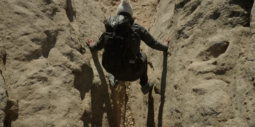 A woman is balancing between two rock walls as she descends to the ground