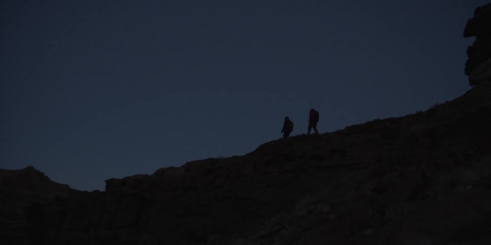 Two hikers walk along a cliff edge at dusk