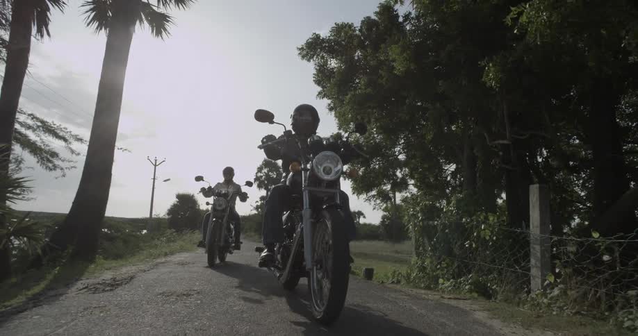 Two men riding motorcycles down a small road