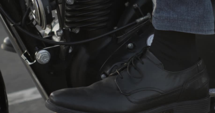 A man's foot rests on the pedal of a moving motorcycles