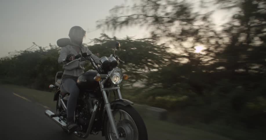 A person is riding a motorcycle down a rode at sunset