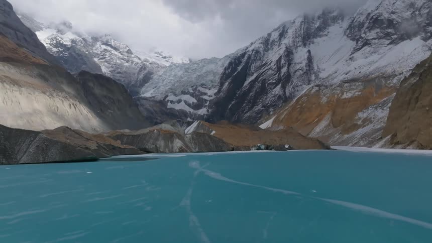 Snowy mountains tower over blue water streaked by ice