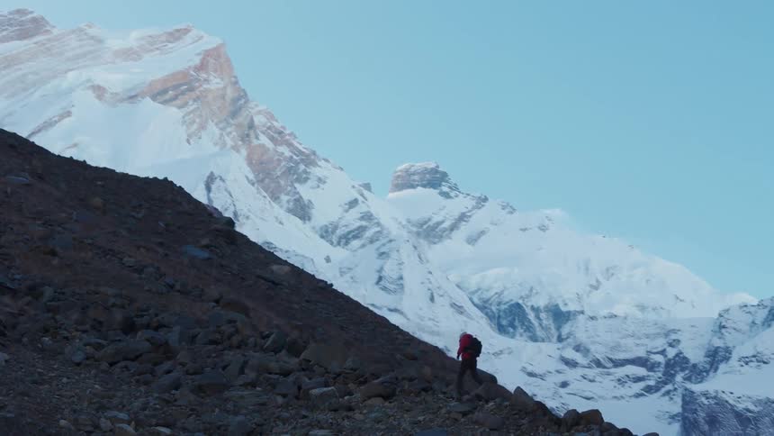 Man hikes up the mountain with an even larger snowy mountain range ahead of him