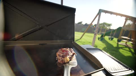 Point of view of a spatula picking up a steak and turning it on the grill plate