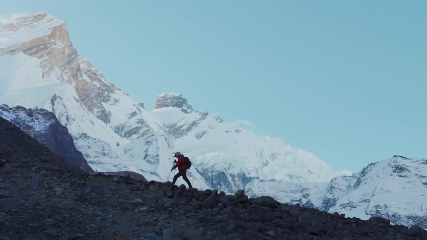 A person hiking on rocky terrain with snow covered mountains in the background