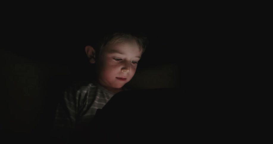 A child reads on a tablet in a dark room