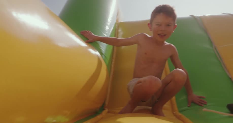 A shirtless little boy is jumping on a green and yellow colored air toy