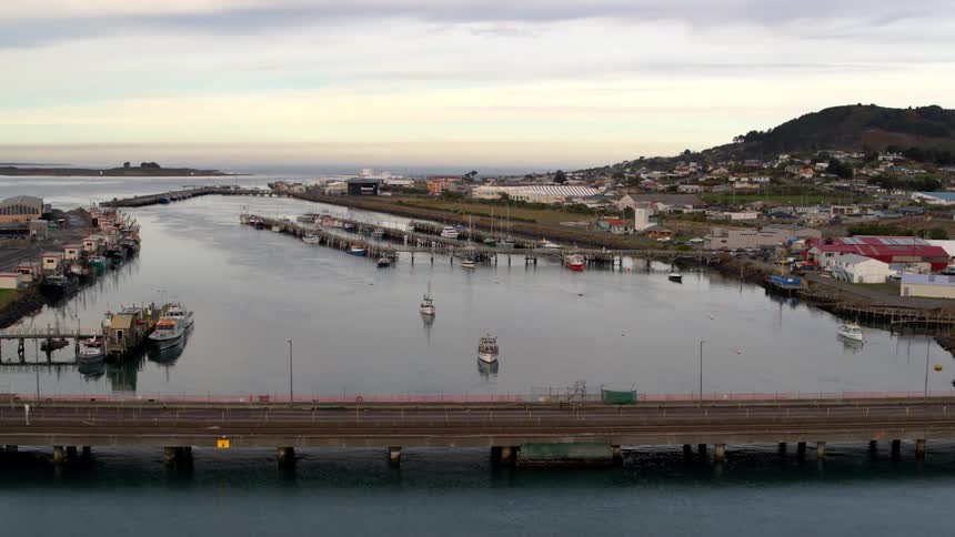 An aerial view of a coastal town with docks boats and buildings lining a river that leads to the ocean