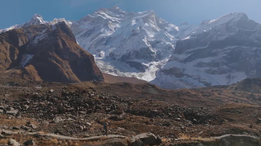 A person is hiking down a rocky trail in front of the mountainous landscape