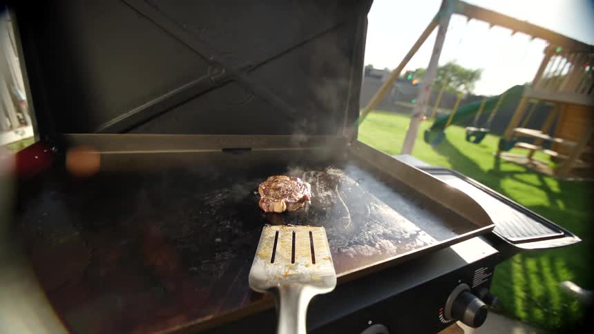 A person moves a steak around on a grill with a spatula