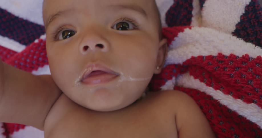 A baby with a milkstained mouth lying on a red white and blue blanket