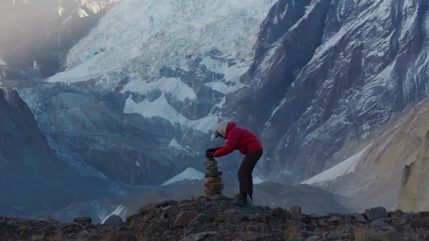 A hiker stacks rocks in a pile on the mountain