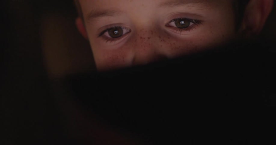 Kid face concentrated on a screen that illuminates his face in a dark environment
