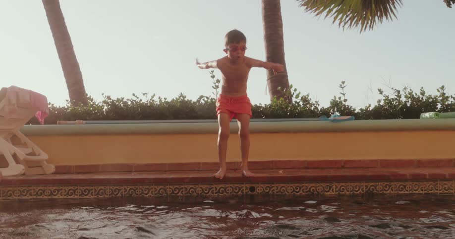 A little boy with his arms raised up preparing to jump into the water of a swimming pool