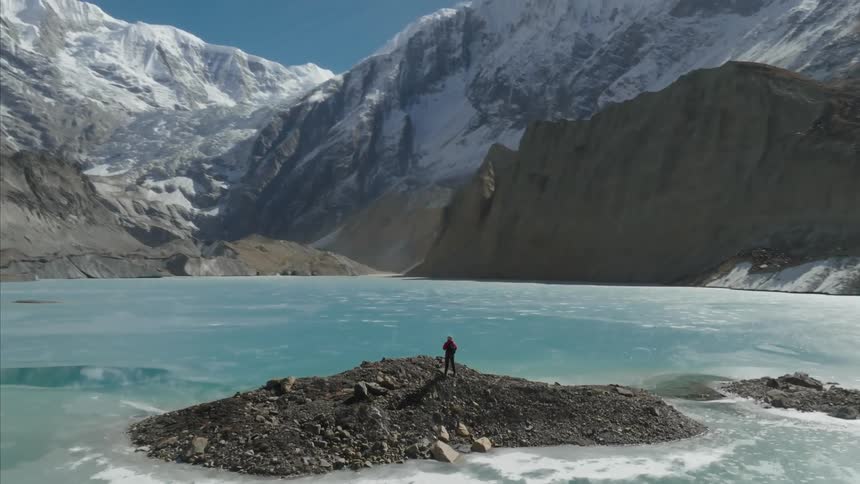 Person in the center of a rock surrounded by a lake and mountains