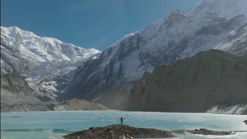 A person stands on a land formation in the middle of an icy lake
